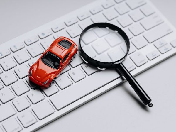 Red toy car on a keyboard with magnifying glass. Symbol of online car review, insurance, purchase.
